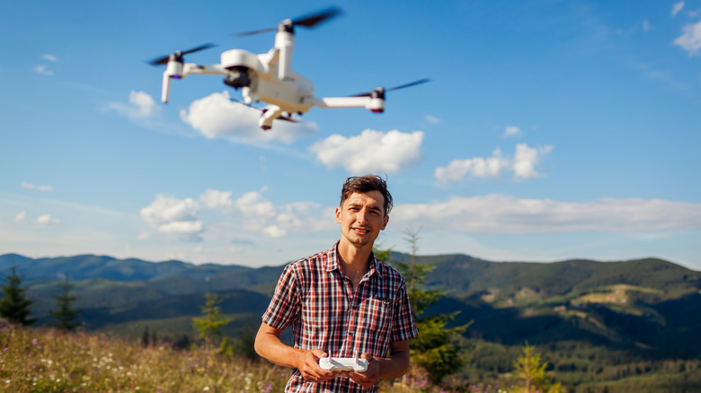 A young man operates a drone in a mountainous area on a sunny day