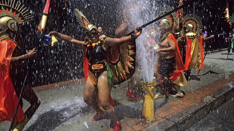 Smiling paraders in carnival outfits next to a blasting fire hydrant in Port of Spain