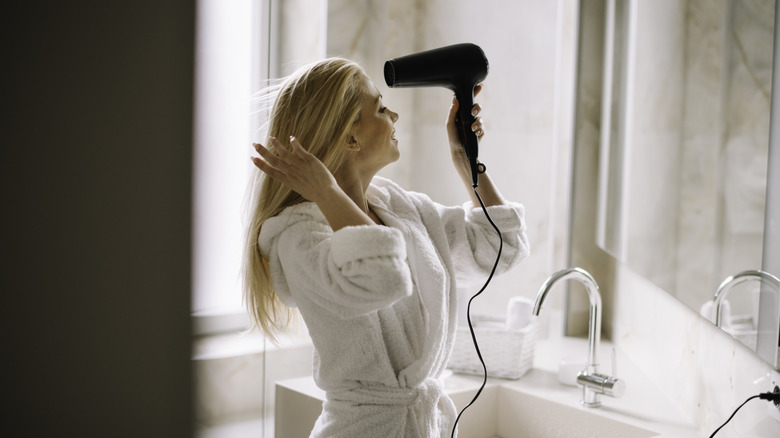 A woman in a robe drying her hair in a hotel bathroom