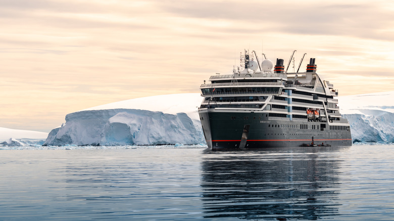A Seabourn Pursuit expedition cruise ship in Antarctica around sunset in calm waters, with bright white icebergs visible in the background