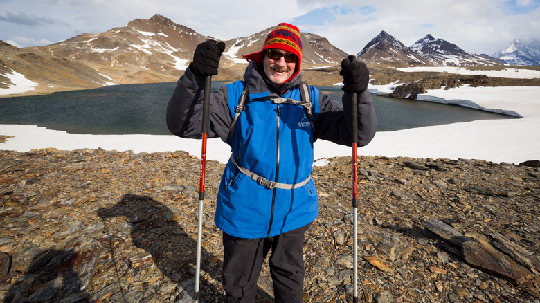 A senior traveler holding walking sticks on a trek on South Georgia Island on a bright day during an Antarctica expedition run by Aurora Expeditions