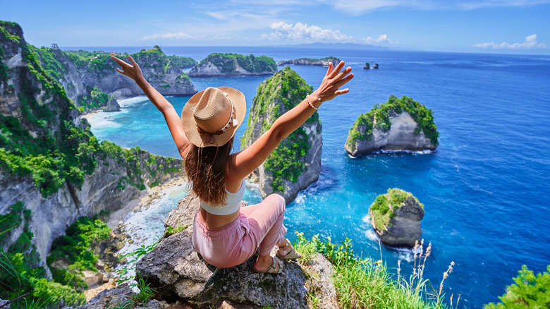 A woman with her hands up sitting in front of a waterscape