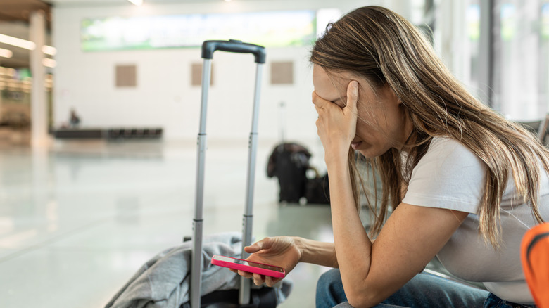 A woman with her head in her hands, holding her phone in front of a suitcase