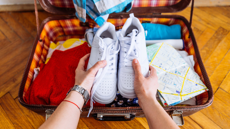 Person holding shoes over open luggage