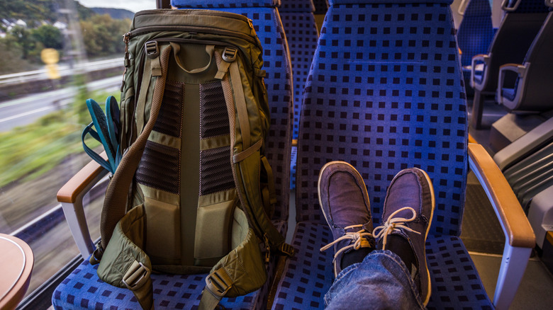 Person on train with feet propped up on seat next to backpack with flip flops in pocket.