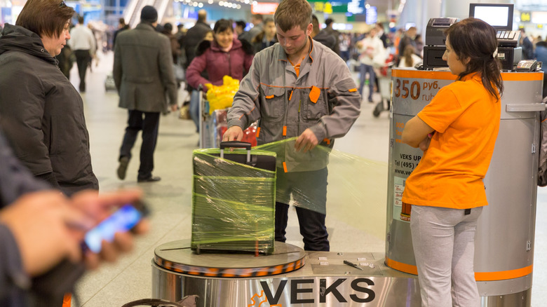 A man wraps a suitcase with plastic at an airport kiosk