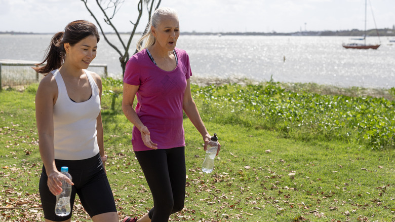 Two women walking by the water on a hot day carrying water bottles