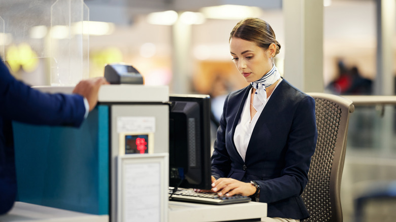 A female attendant at an airline customer service desk at the airport types on her computer