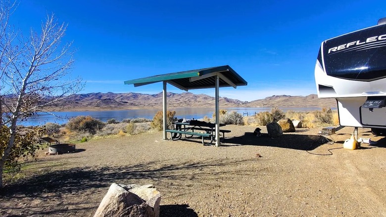 Partial view of an RV at a waterfront campsite at Wild Horse State Recreation Area in Nevada, featuring a shaded picnic area and a fire pit.