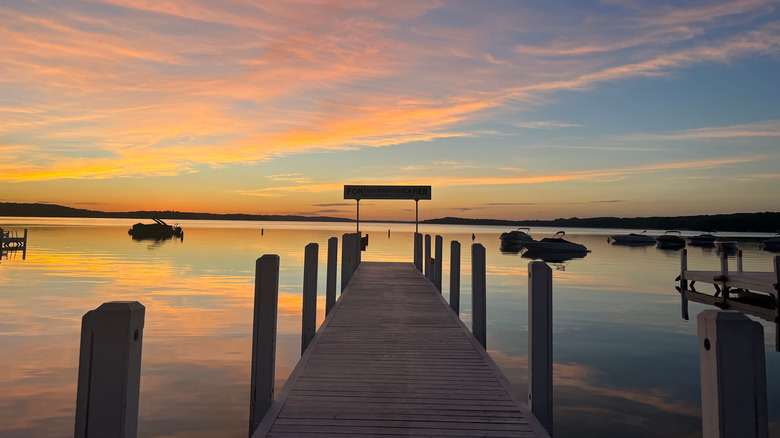 A silhouette of a dock going into Geneva Lake at sunset with clouds overhead reflecting off the calm water