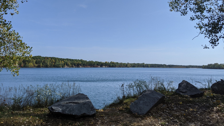 Wazee Lake from shore with stones on a path, calm blue water, and the opposite shore in the distance