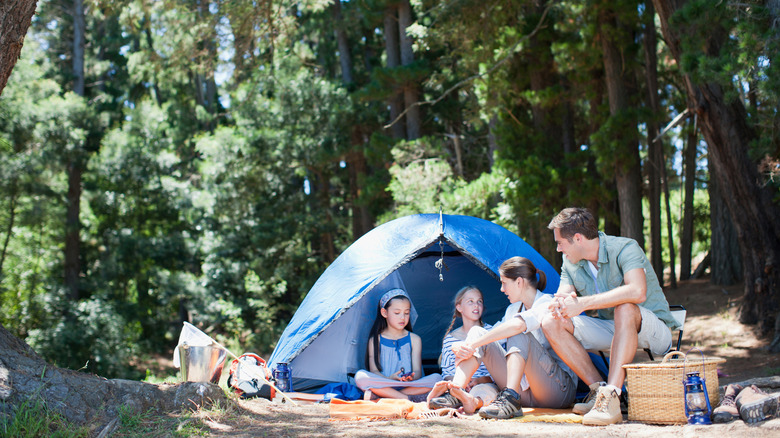 Young parents with two girls sitting in front of a tent