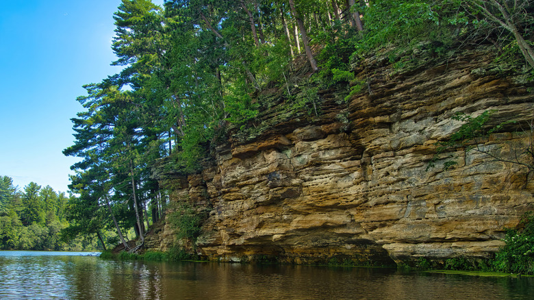 The calm lake with a rocky cliff topped with tall trees