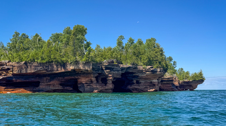 sea caves carved into Devils Island's shore on a clear day, with the water looking teal in the sunlight