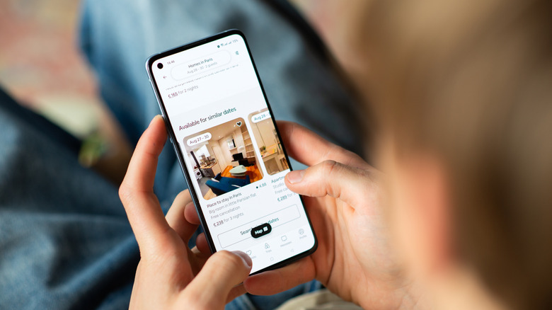 Close-up image of a pair of hands holding a smartphone with an Airbnb page onscreen.
