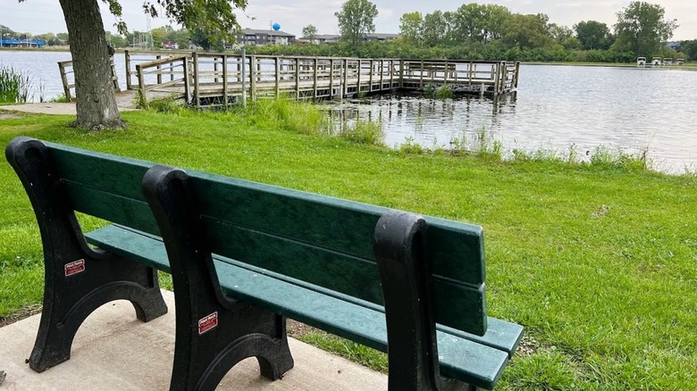 A park bench on the shore of a scenic lake in Mukwonago, Wisconsin, with a pier going into the water.