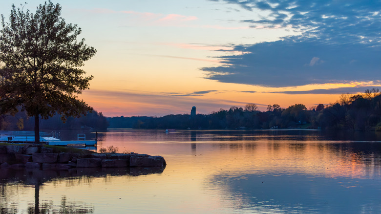 Sunset over a river, with an embankment and a dock on the foreground.