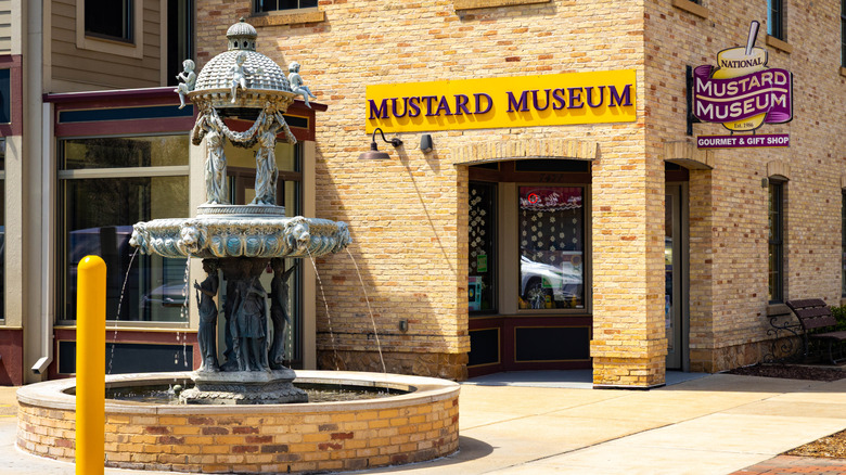 A Mustard Museum sign and logo on a yellow building behind a fountain