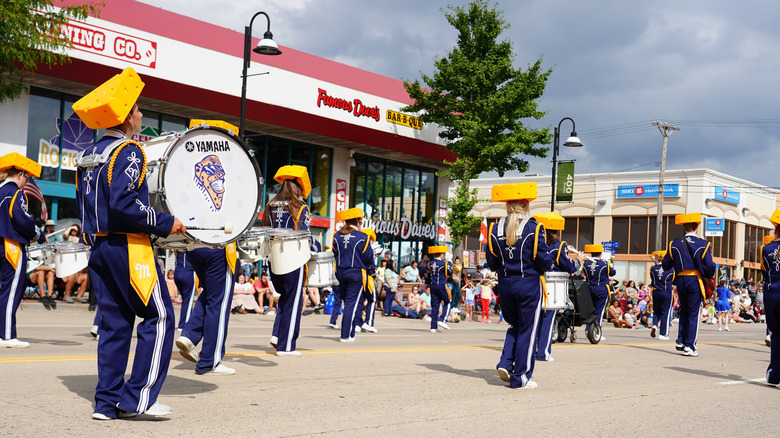 A band marches in a cheese festival parade with foam cheese on their heads