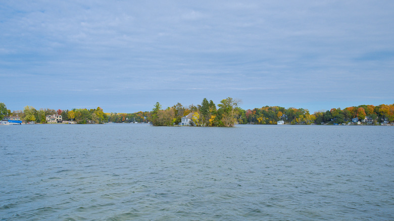 A house on Lone Island in the middle of Big Cedar Lake during the fall season with other houses and lots of trees in the background.