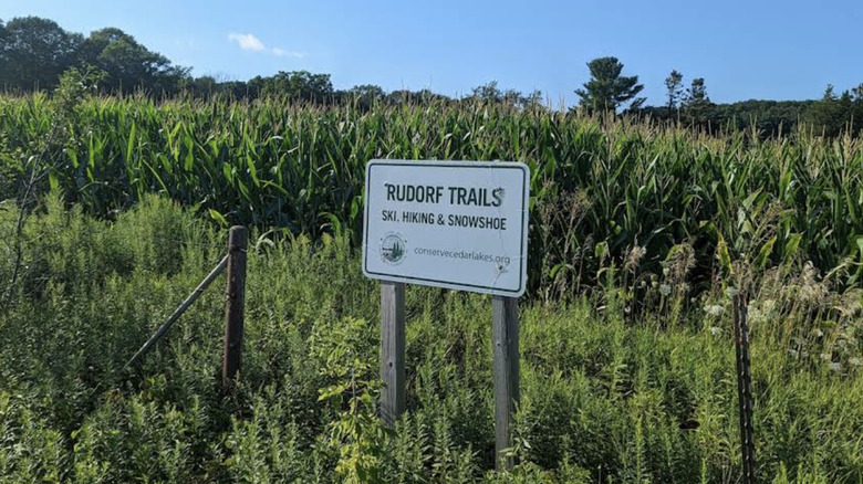 A sign that says Rudorf Trails with a cornfield behind it.
