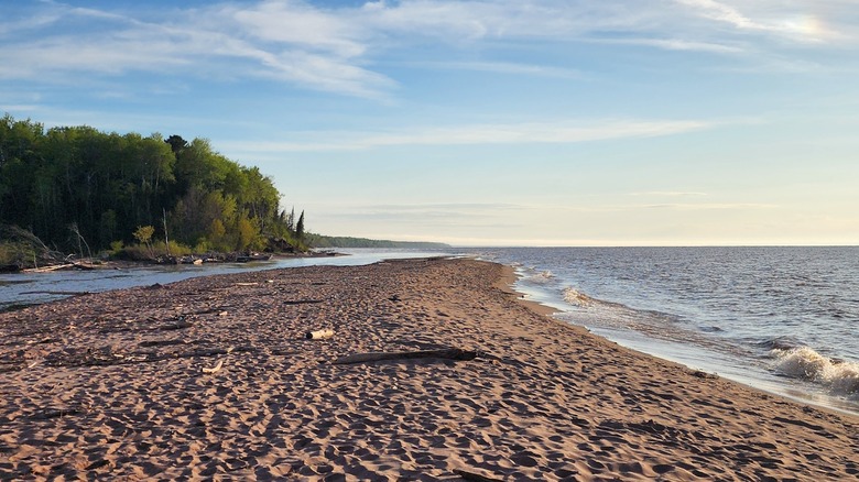 A long Lake Superior beach with the mouth of the Brule River, pine trees, and the lake to the right side stretching to the horizon
