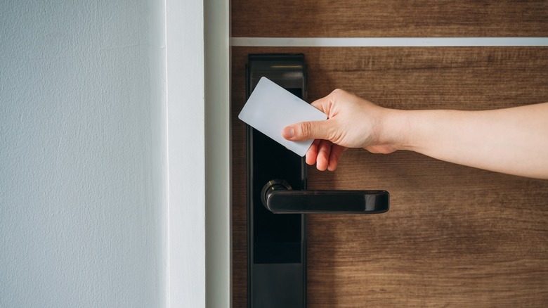 a hand holds a keycard to a hotel room door