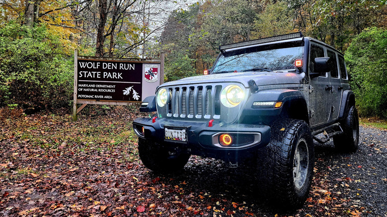This is a picture of a sign for Wolf Den Run State Park along with a Jeep.