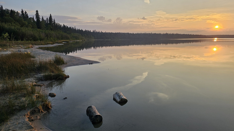 Sunset at Pine Lake, with trees along the shoreline, at Wood Buffalo National Park