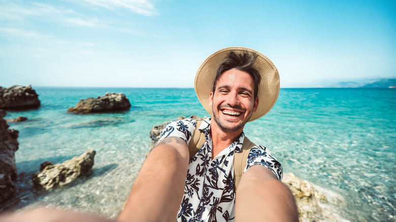 Happy man taking selfie with smart mobile phone on a beach.
