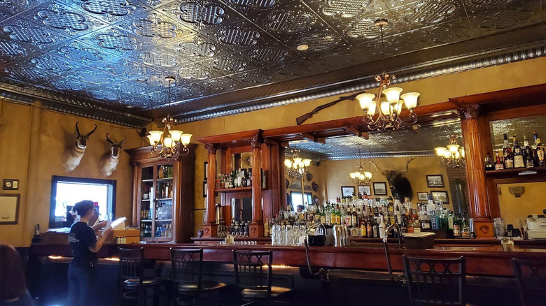 A cherrywood bar with mirror, moose heads and mirrors on the walls, and decorative tin ceilings