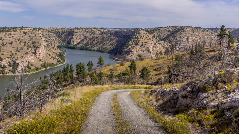 A road along prairies, hills and a lake in the background