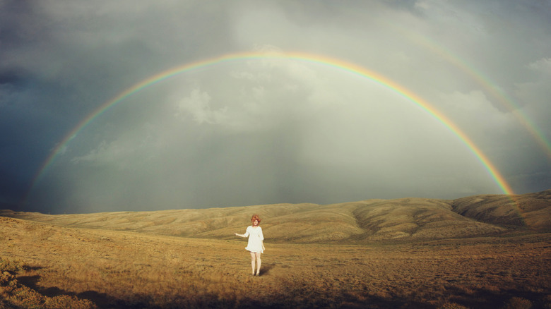 A woman standing in a field under a rainbow in the sagebrush plains in Rawlins, Wyoming.