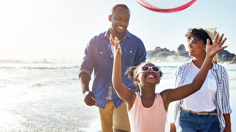 Two smiling parents and a happy child walk along the beach
