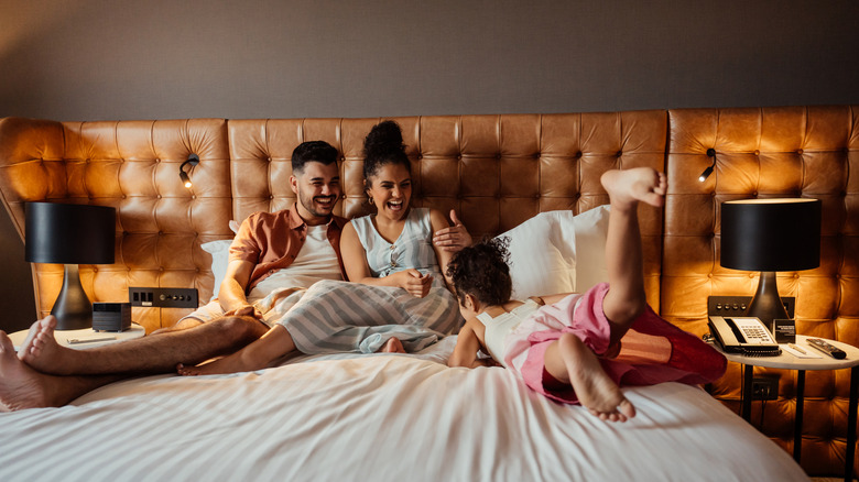 A family of three lounging in a hotel room bed