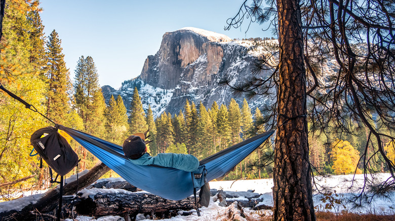 A man reclines in a blue hammock in the shadow of Half Dome in Yosemite during winter