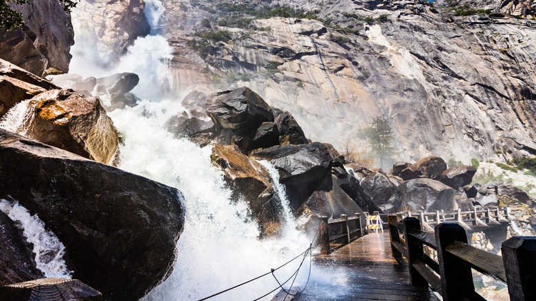 A waterfall surges over a wooden bridge