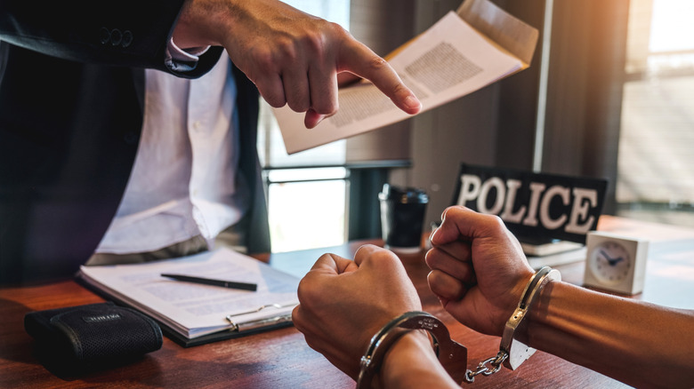 A closeup of hands and a pointing finger, with one person handcuffed while being interrogated by the police