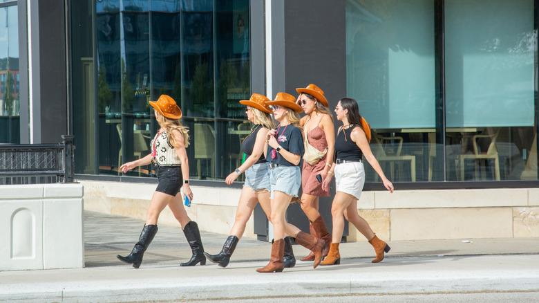 A group of young women walking along the street in Nashville while wearing matching cowboy hats and boots