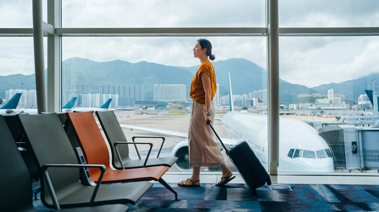 A woman walks through an airport with a carry-on suitcase