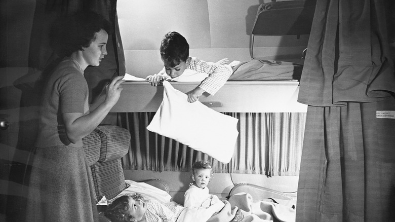 A mother puts her children to bed in overhead and in-seat berths on a Boeing 377 Stratocruiser.
