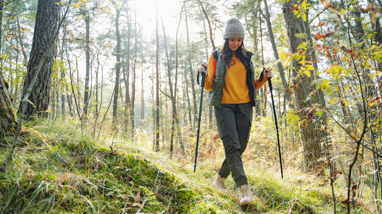 A female hiker is walking through the woods, holding her trekking poles incorrectly by not using the strops