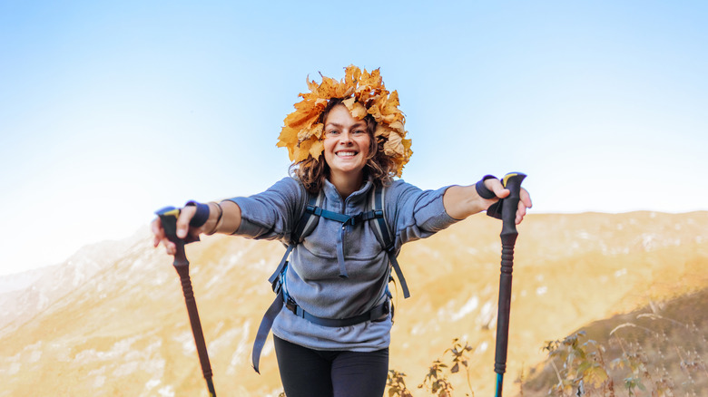 A female hiker wearing a wreath of autumn leaves holds her hiking poles forward, displaying the correct way to use the attached straps