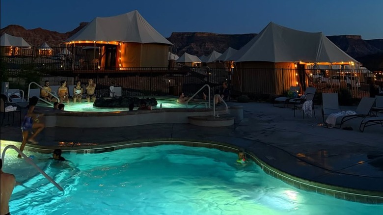 Nighttime view of swimming pool and hot tub surrounded by lounge chairs and luxury glamping tents at Zion Wildflower Resort near Zion National Park in Utah