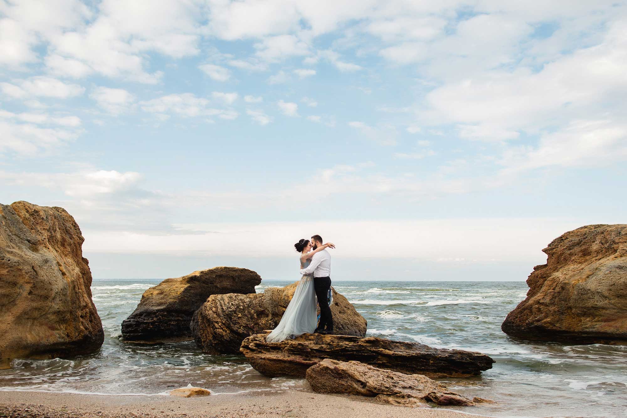 Newlywed couple standing on rock on the beach