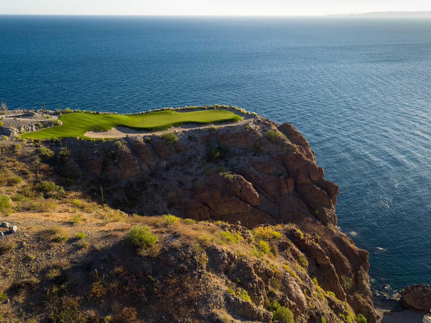 A golf course overlooking the ocean on a hillside.