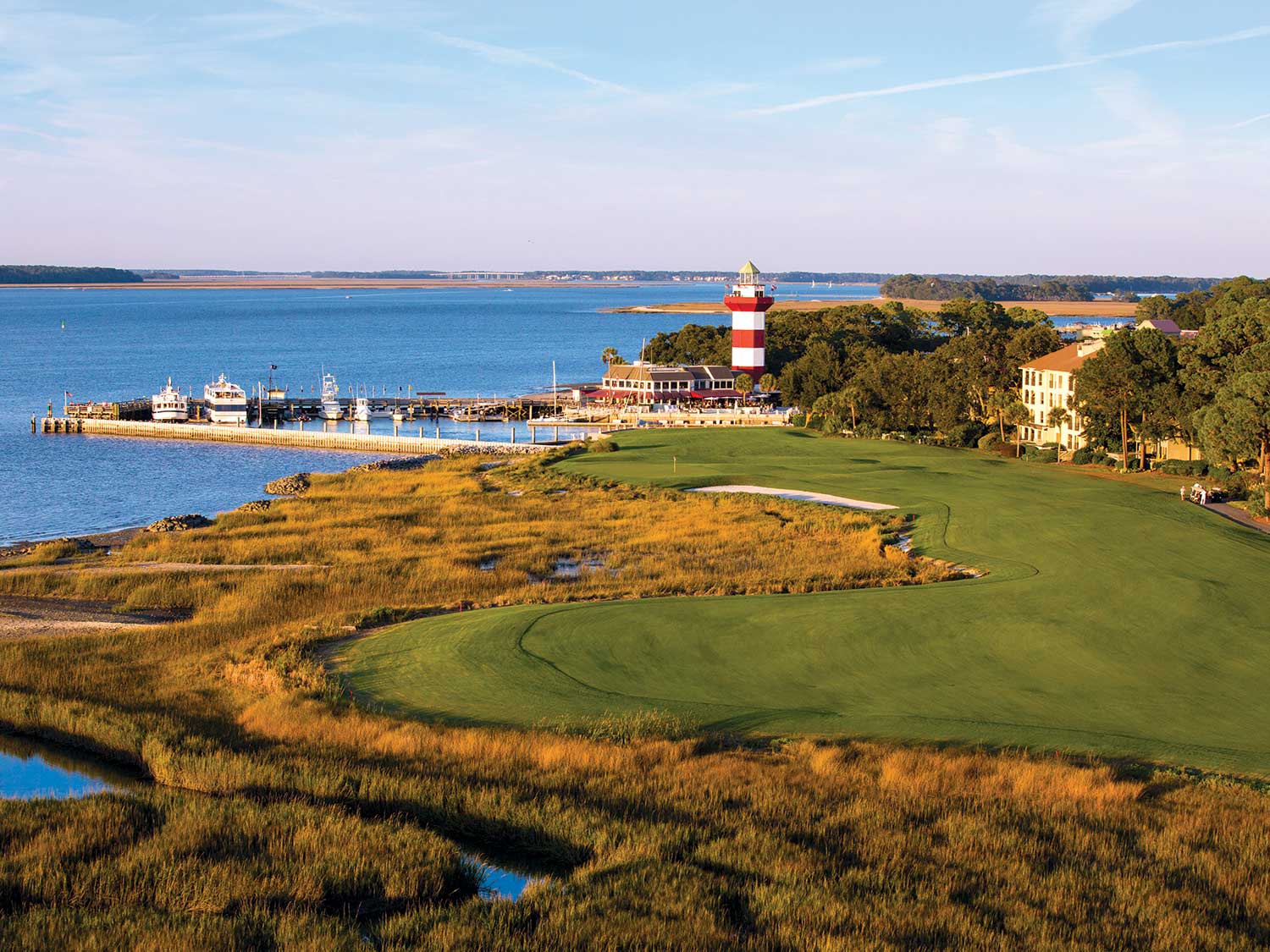 A lighthouse by a pier next to a waterfront golf course.