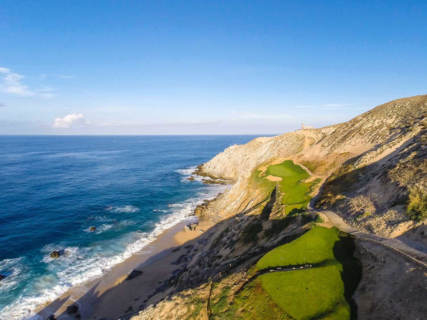 A hillside golf course next to a beach and hillside.