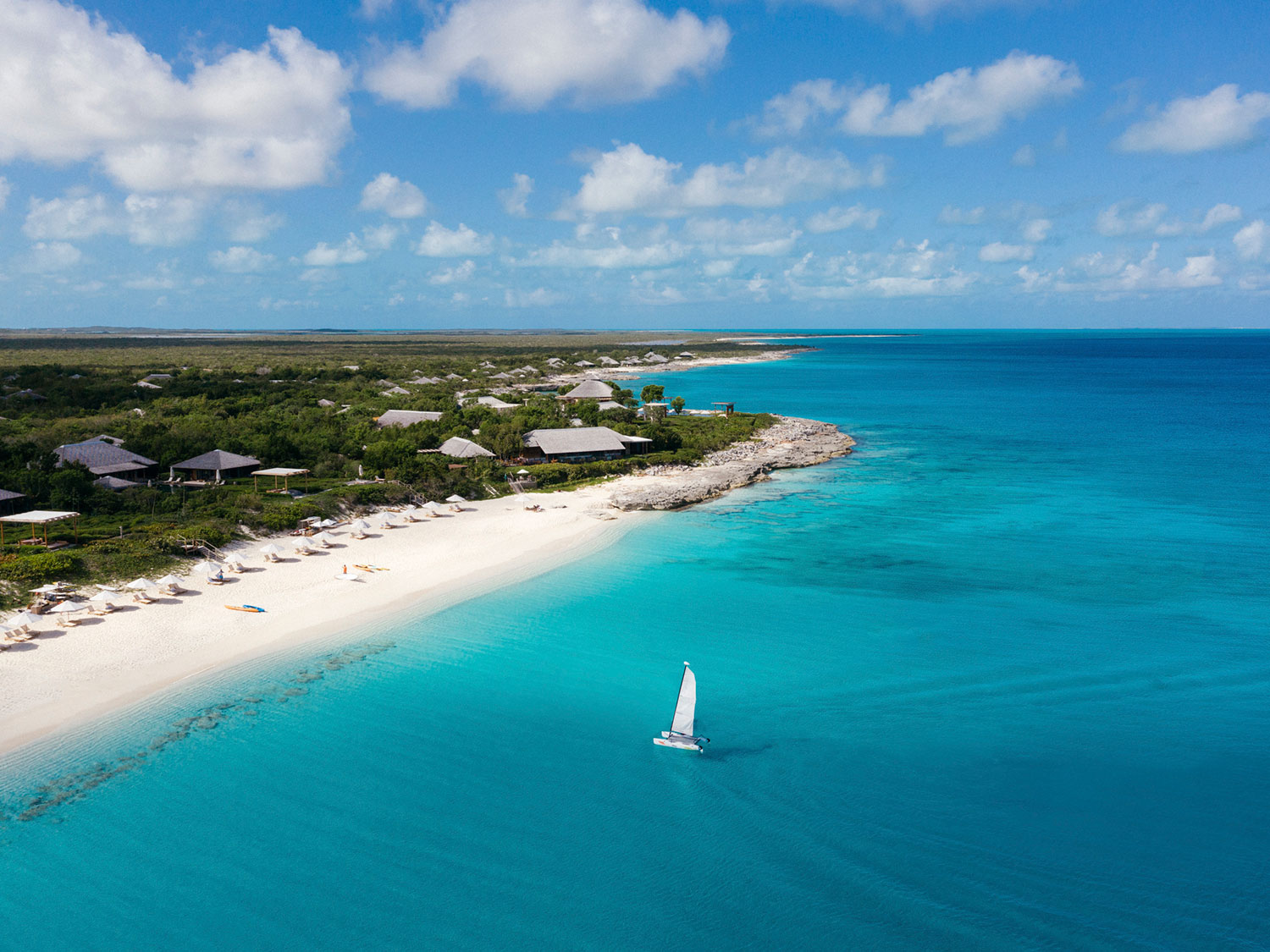 An aerial view of a sailboat off the shore of the beach.