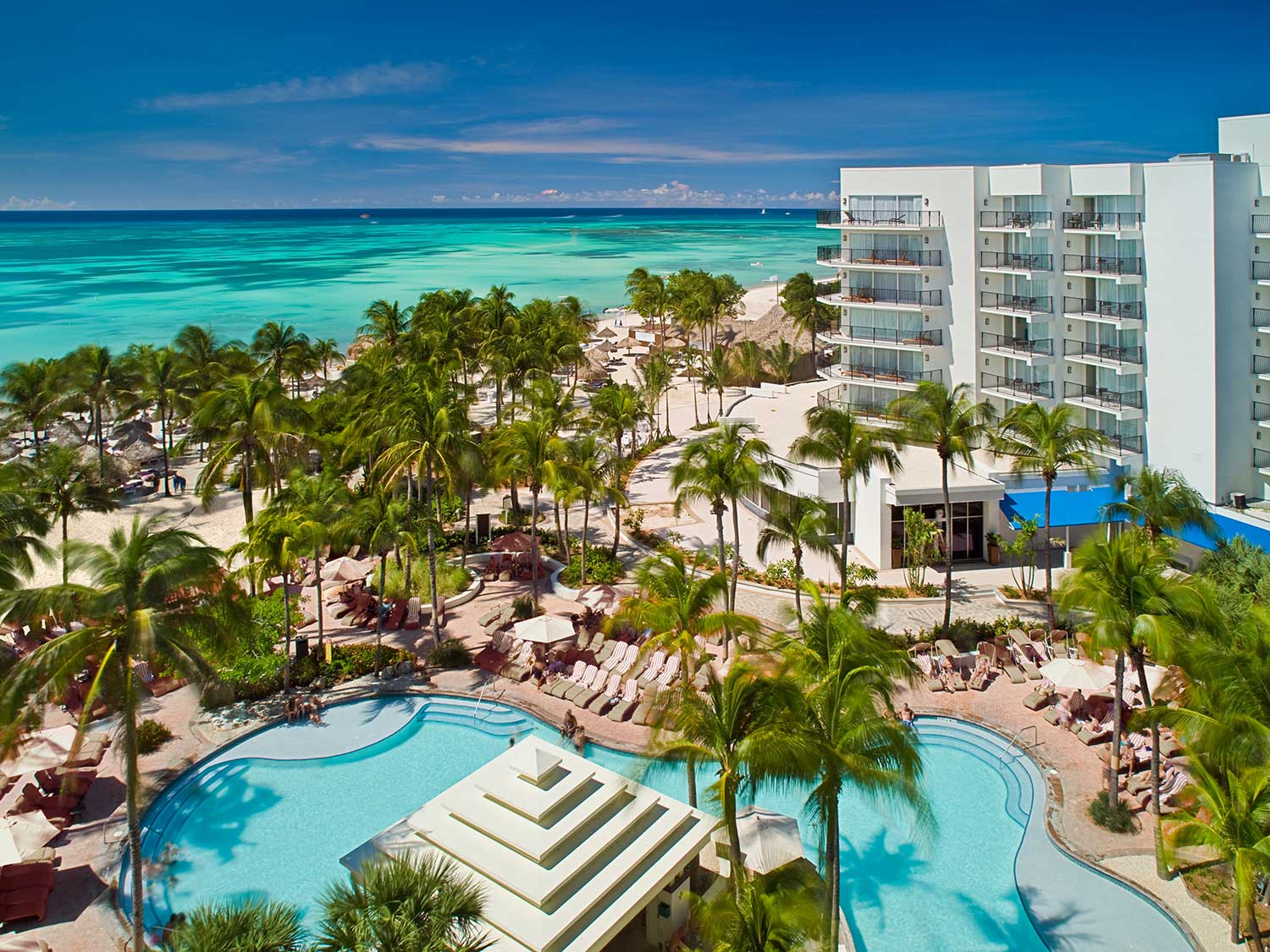 An aerial photo of a beach resort in Aruba, surrounded by palms, pools, and open waters.